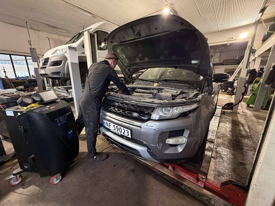 Механик у автомобиля с открытым капотом на подъёмнике в мастерской